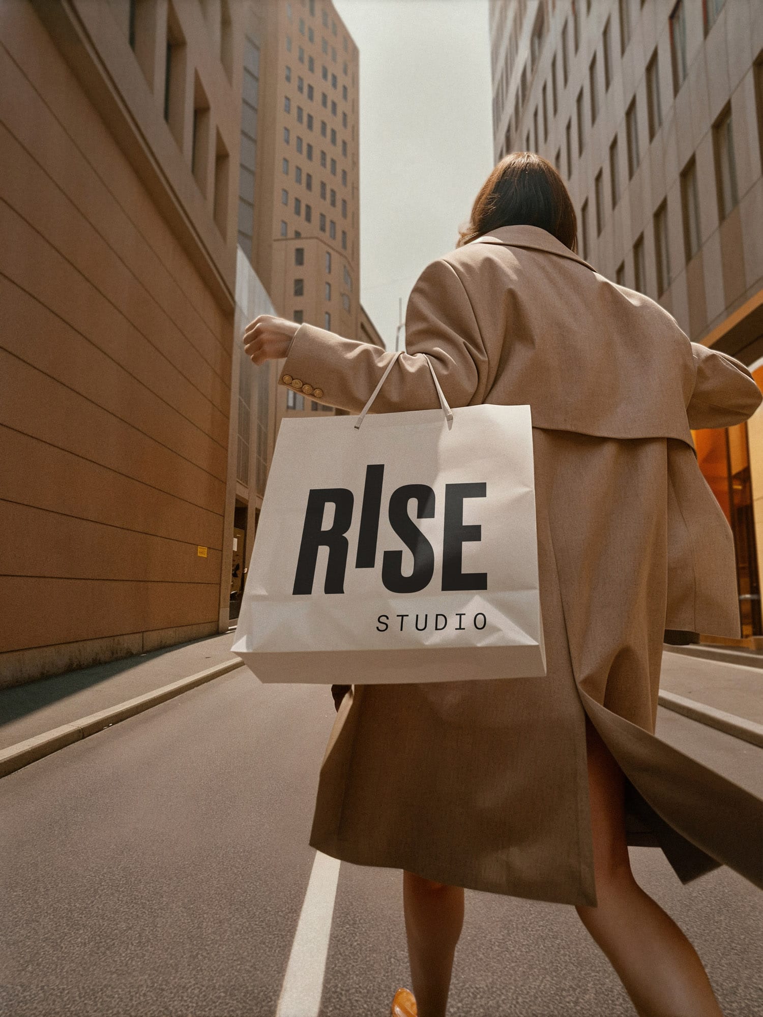Person trägt eine weiße Papiertasche mit dem RISE Studio Logo durch eine urbane Straße