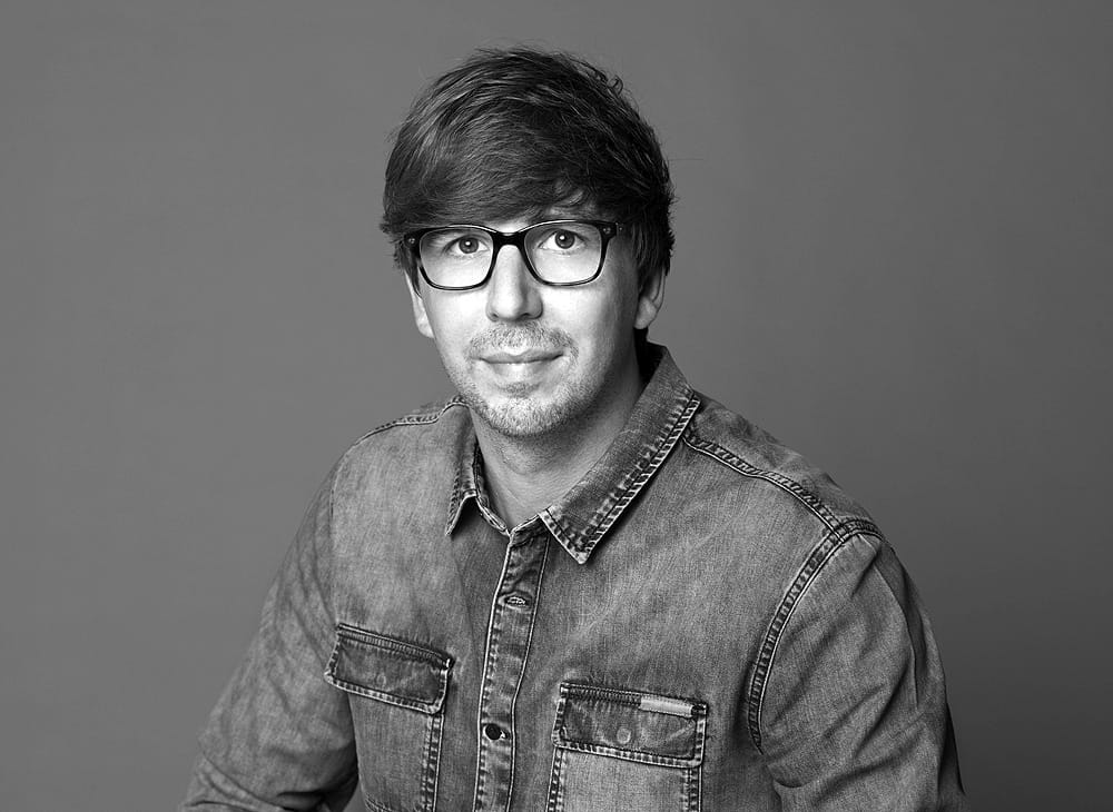 Porträtfoto von Björn Sander – lächelnder Mann mit Brille und Jeansjacke