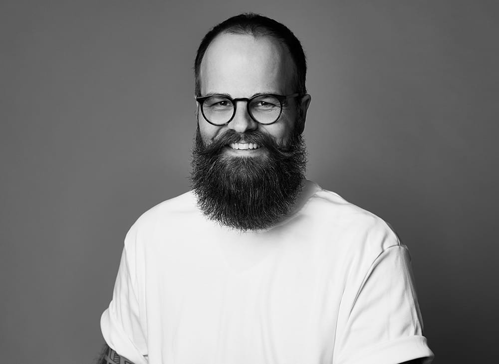 Porträtfoto von Florian Dylus – lächelnder Mann mit Vollbart und Brille in weißem T-Shirt