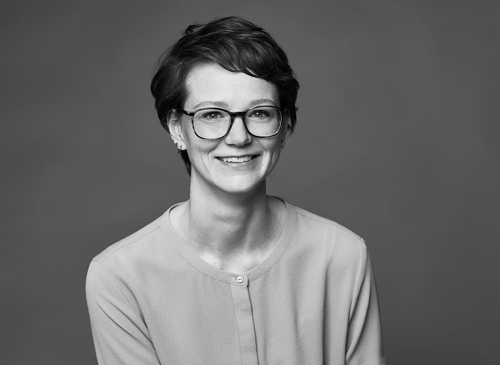 Porträtfoto von Katarina Gier – lächelnde Frau mit kurzen braunen Haaren und Brille in hellem Cardigan