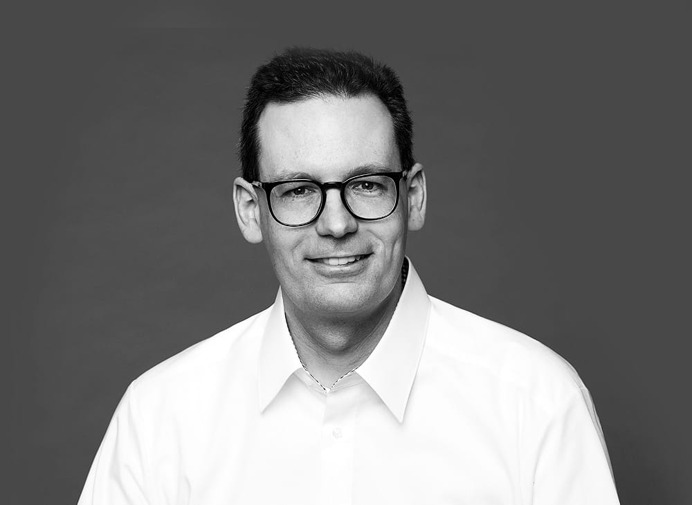 Porträtfoto von Marcell Vorreier – lächelnder Mann mit Brille und weißem Hemd