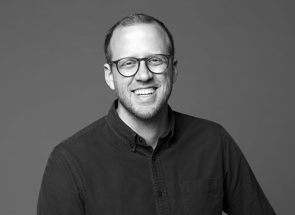 Porträtfoto von Maxime Bürger – lächelnder Mann mit Brille und dunklem Hemd