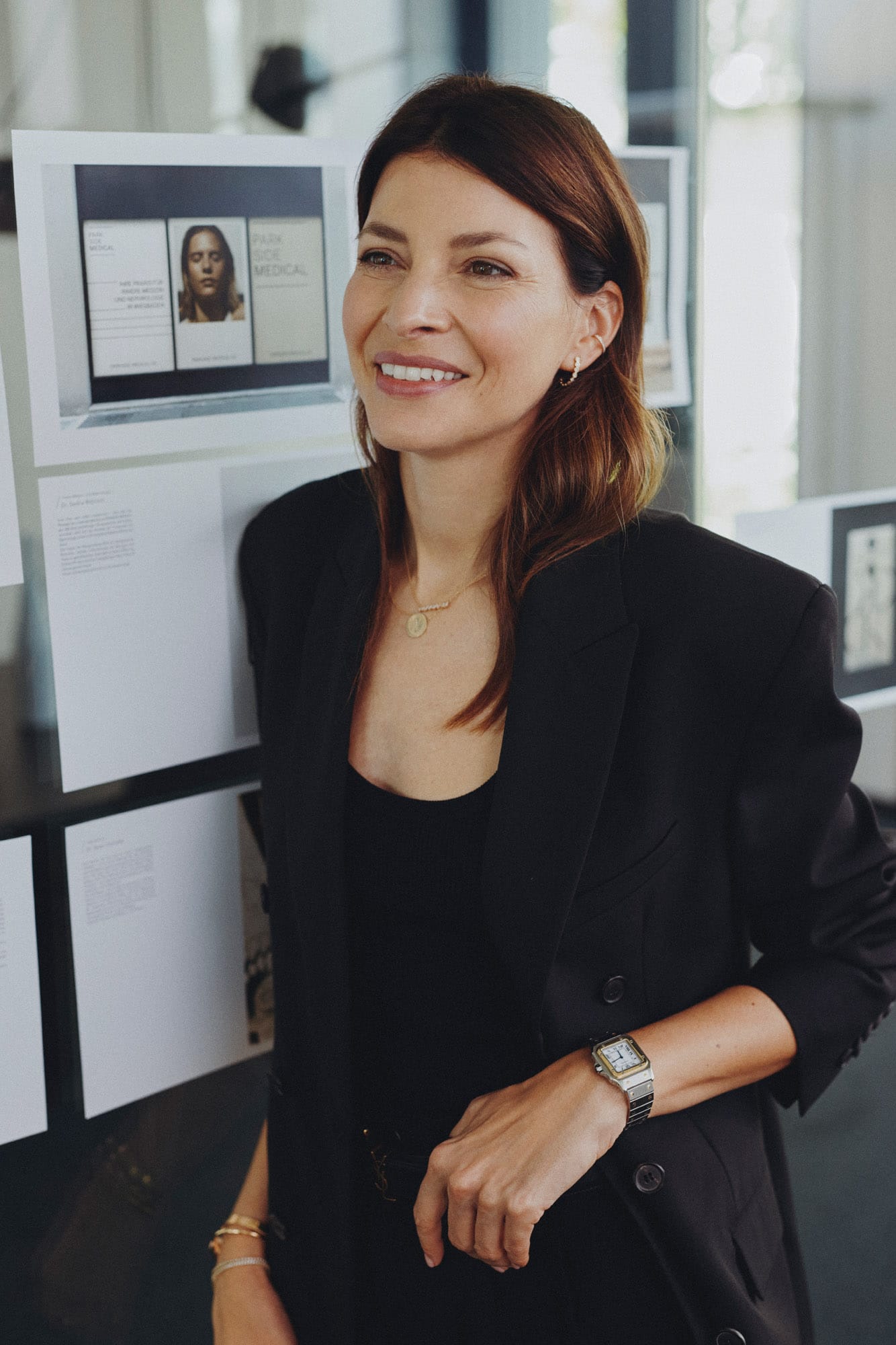 Lächelnde Frau in schwarzem Blazer steht vor einem Moodboard in einem modernen Büro